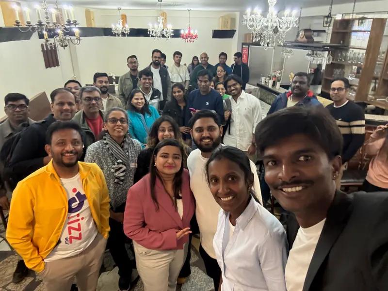 A large group of attendees pose together for a photo at the end of an indoor event, smiling at the camera.