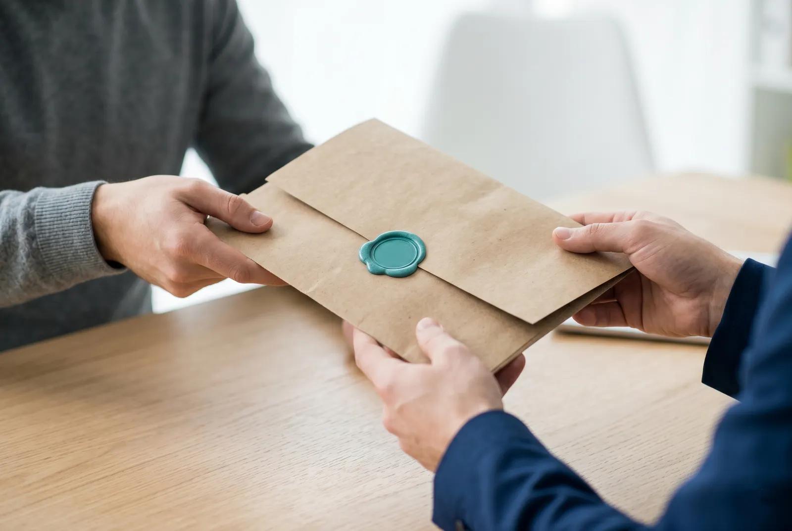 An adviser handing a sealed document envelope to a client across a desk