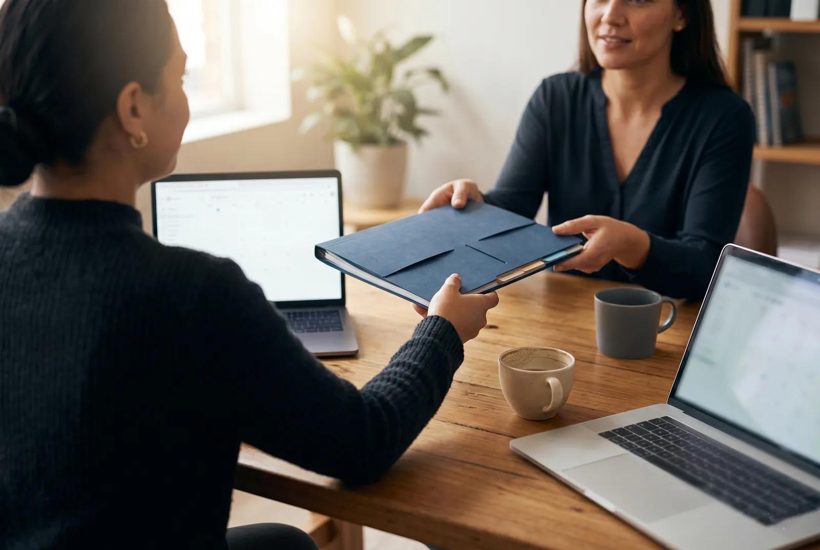 Two people in a consultation handing over a document folder